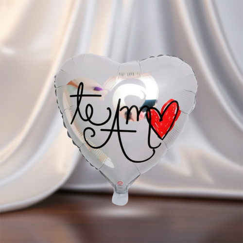 Globo plateado en forma de corazón con la frase te amo y un corazón rojo dibujado, sobre fondo de tela blanca difuminada