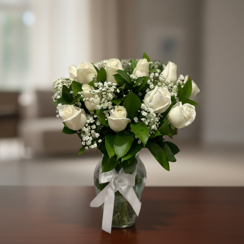 Ramo de rosas blancas con paniculata y hojas verdes en jarrón de cristal con lazo blanco sobre mesa de madera