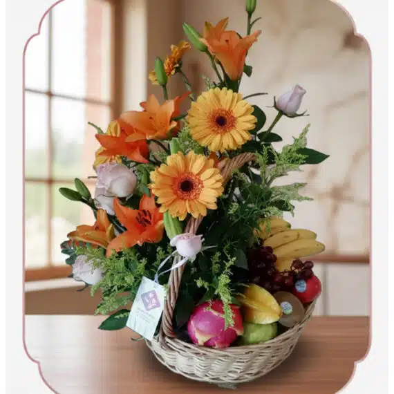 Arreglo Basilio: Cesta Frutal con Rosas y Lirios Frescos Cesta de mimbre con arreglo floral de rosas, lirios y gerberas, acompañada de frutas frescas como plátanos, uvas, manzanas y