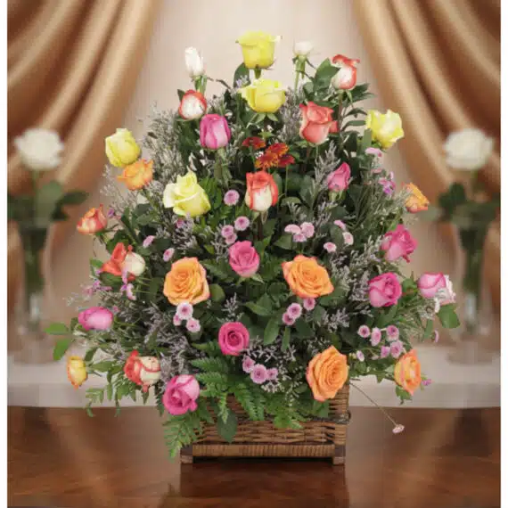 Arreglo floral DONNIA en cesta de mimbre con 34 rosas de colores variados (rosas, amarillas, naranjas) y follaje verde, sobre