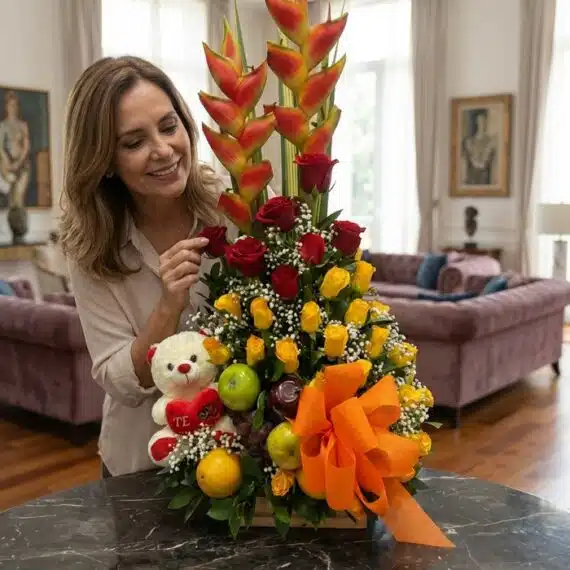 Mujer elegante admirando un Arreglo Floral con Frutas Encanto, compuesto por rosas rojas y amarillas, heliconias, frutas fres