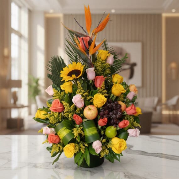 Exquisito Arreglo Floral con Frutas Tropicales para Decoración Elegante Arreglo floral vibrante con rosas amarillas y salmón, girasol, ave del paraíso y frutas tropicales como uvas, manzana y lima,