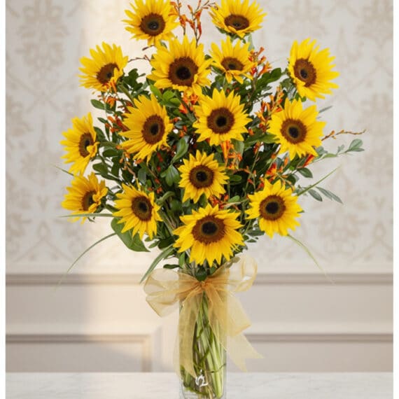 Arreglo Floral de Girasoles LENU: Radiante Belleza para Tu Hogar Arreglo floral de girasoles LENU en un jarrón de cristal con lazo dorado, sobre una mesa de mármol y fondo elegante.