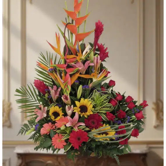 Arreglo Floral IDARA: Diseño Exclusivo con Rosas y Flores Exóticas Arreglo floral IDARA con rosas rojas, girasoles, lirios, heliconias y jengibre rojo en un fondo elegante y bien iluminado.