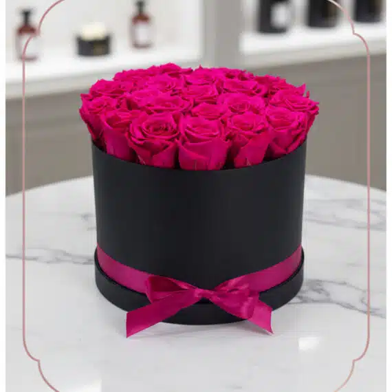 Arreglo Floral Marena: Rosas Fucsia Vibrantes en Caja Negra Elegante Arreglo Floral Marena con 21 rosas fucsia vibrantes y frescas en una caja redonda negra con lazo fucsia, sobre una mesa de má
