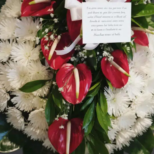 Detalle macro de la Corona Fúnebre Trinidad con anthuriums rojos vibrantes, crisantemos blancos puros y follaje verde, con ro