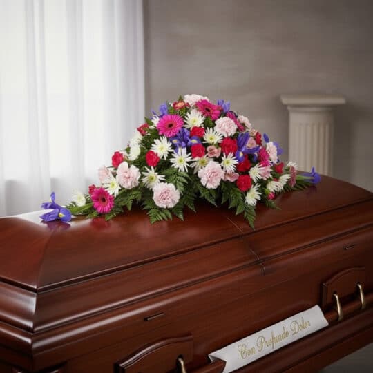 Cubre caja fúnebre 'El Legado de Francisco' con flores variadas en tonos rosas, blancos, rojos y azules, sobre un ataúd de ma